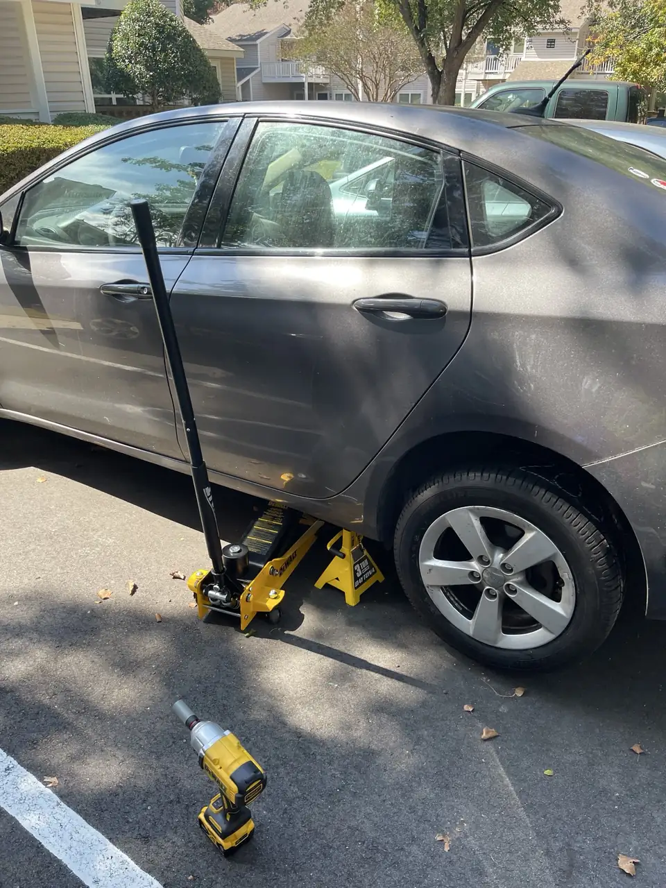 Amp Rescue technician's jack and impact wrench under a sedan's front wheel in a Triangle parking lot